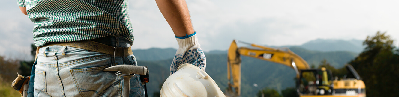 construction guy who is wearing construction belt and helmet with bulldozer in background